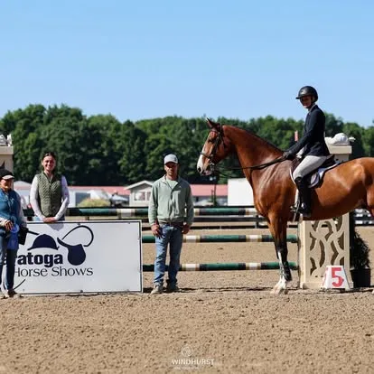 Rider on bay horse beside Saratoga Horse Shows sign in ring
