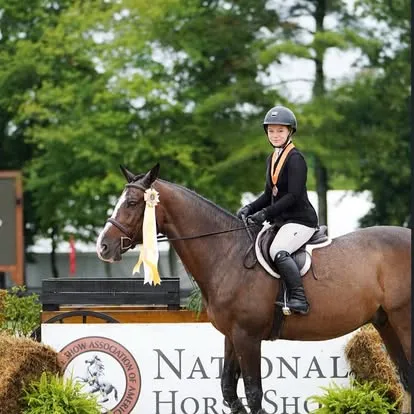 Young rider on bay horse with yellow ribbon at National Horse Show