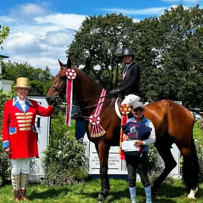 Ringmaster in red coat presents rider on bay with red ribbons