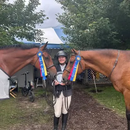 Rider holding two horses flanked by blue tricolor championship ribbons