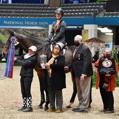 Rider on dark horse with trophy and ribbons at National Horse Show