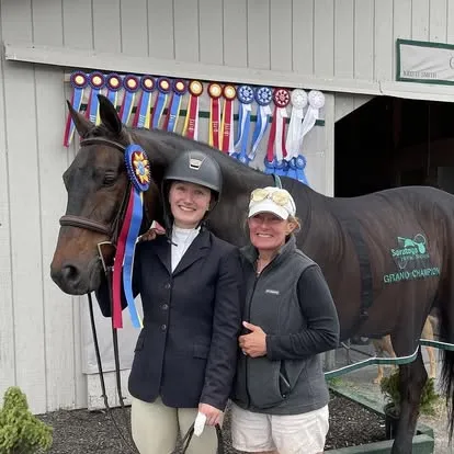 Two women and horse beneath wall of many ribbons
