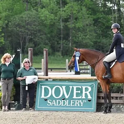 Rider on bay horse jumping beside Dover Saddlery ring banner