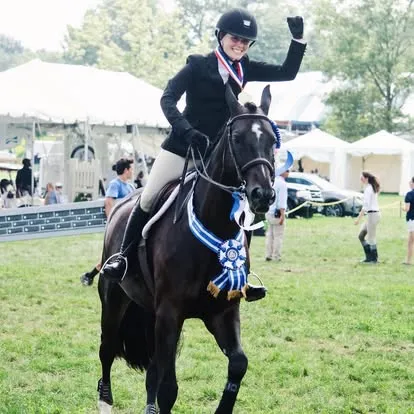 Rider raises fist on dark horse with blue championship ribbons