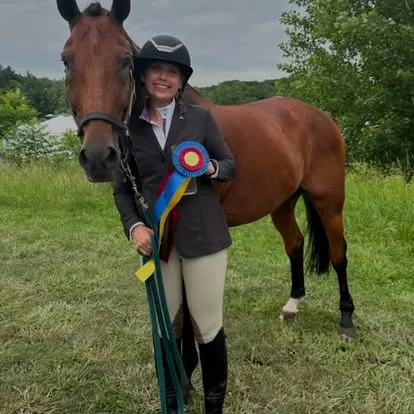 Rider holding tricolor ribbon standing with bay horse in grassy field