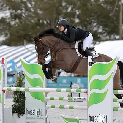 Rider on bay horse over green Horseflight branded jump standards
